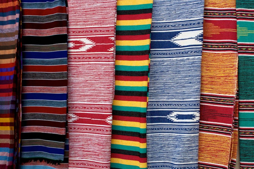 Colorful striped woven rugs hanging side by side in red, blue, yellow, green and orange with diamond patterns