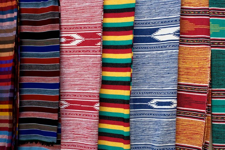Colorful striped woven rugs hanging side by side in red, blue, yellow, green and orange with diamond patterns